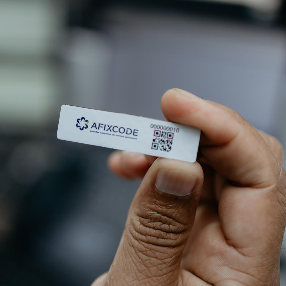 Mão segurando etiqueta de identificação patrimonial Afixcode com QR code para controle e rastreamento de ativos