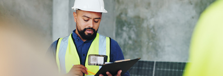 Engenheiro com capacete e colete analisando tablet durante avaliação civil em obra ou estrutura industrial